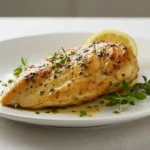 Cava Chicken Recipe 7 Bold Flavors For The Ultimate Meal! 11 A beautifully styled plate with a golden-brown and tender Cava chicken breast from the Cava Chicken Recipe, garnished with fresh herbs and a wedge of lemon. The chicken is presented on a simple white plate, with soft lighting highlighting the vibrant marinade and juicy texture, emphasizing the Mediterranean flavors in a clean, minimalist setting.