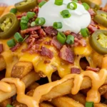 Loaded French Fries Recipe topped with cheese, bacon, sour cream, and green onions.