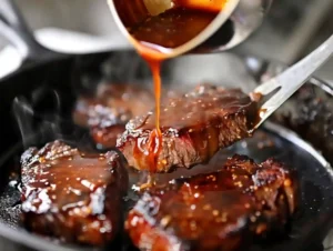 Teriyaki sauce being poured over seared steak with sauce bubbling and caramelizing in pan for teriyaki beef steak recipe