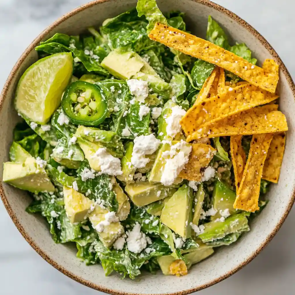 Mexican Caesar Salad 6 A served Mexican Caesar Salad topped with tortilla strips and lime wedge on a white marble surface.