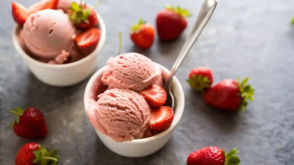 Two white bowls filled with strawberry ice cream and fresh sliced strawberries on top