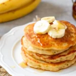 Brown Sugar Banana Pancakes stacked on a plate with sliced bananas and syrup