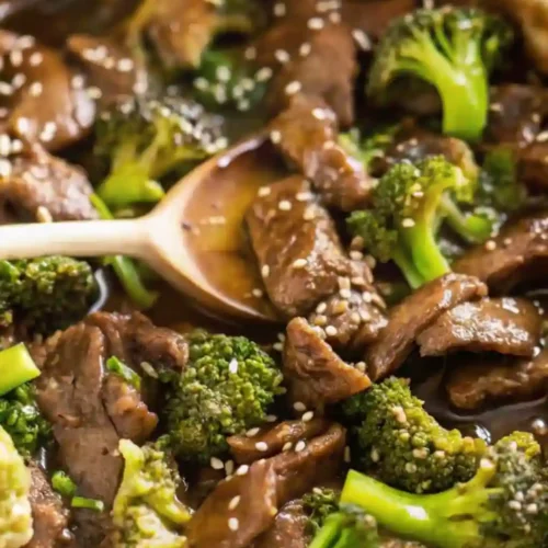 The Best Takeout-Style Chinese Beef and Broccoli Stir Fry 10 Chinese beef and broccoli served in a deep pan with wooden spoon and sesame seeds