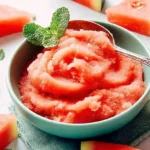Bowl of homemade watermelon sorbet with mint and sliced watermelon