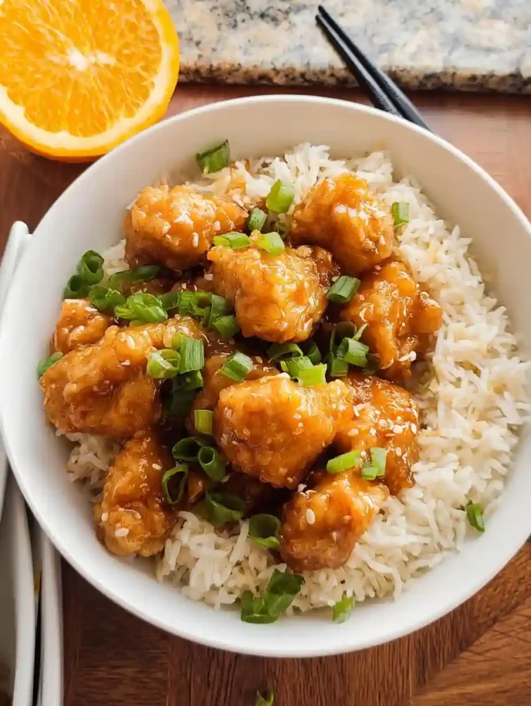 Easy Gluten-Free Orange Chicken (Better Than Takeout!) 2 Overhead view of gluten-free orange chicken served on white rice with scallions in a white bowl