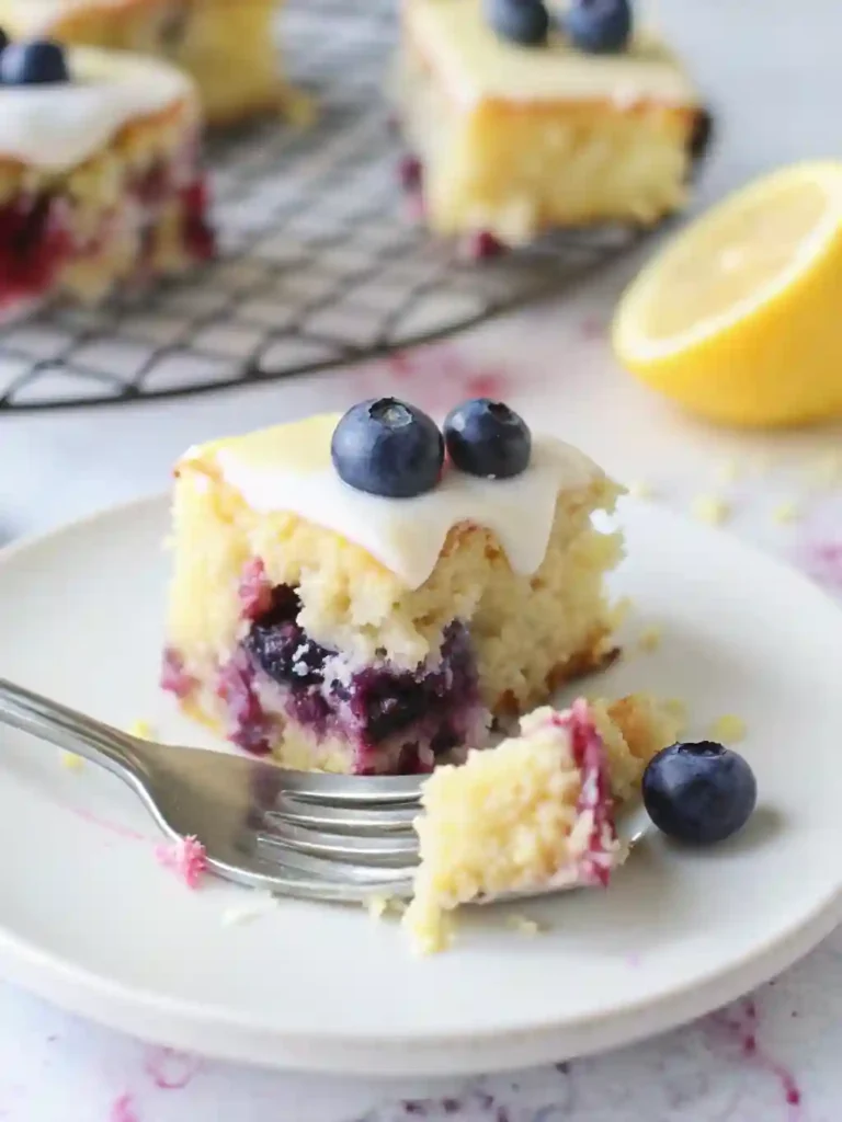Lemon Blueberry Sheet Cake Recipe 6 Lemon blueberry sheet cake with glaze and a fork holding a bite-sized piece in front of a cooling rack