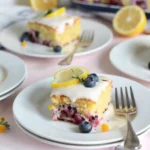 A slice of lemon blueberry sheet cake topped with lemon glaze, a lemon slice, and fresh blueberries