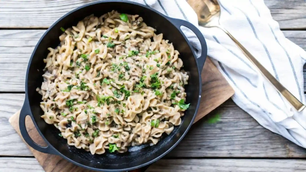 Skillet of creamy ground beef stroganoff topped with herbs on rustic wooden table