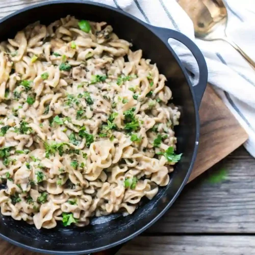 Skillet of creamy ground beef stroganoff topped with herbs on rustic wooden table