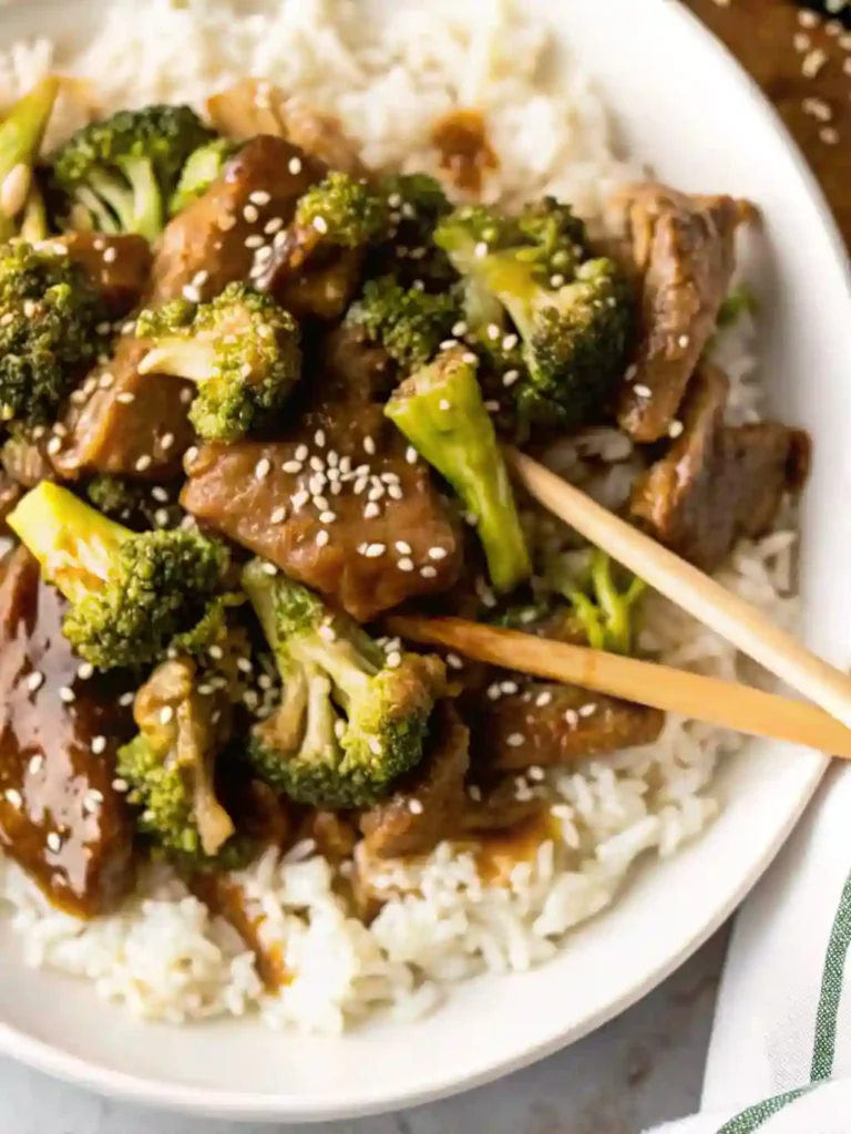 The Best Takeout-Style Chinese Beef and Broccoli Stir Fry 9 Top view of Chinese beef and broccoli with chopsticks and sesame seeds on steamed rice
