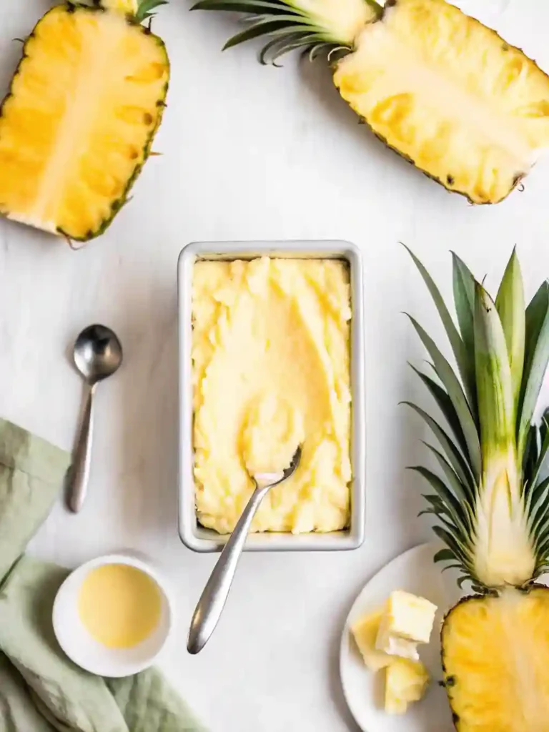 5-Star Pineapple Ice Cream Recipe You'll Crave 7 Homemade pineapple ice cream in a metal container with spoon and fresh pineapple halves