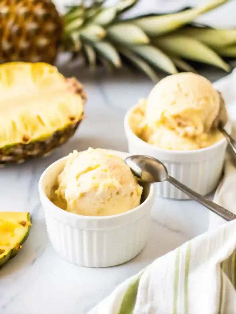 5-Star Pineapple Ice Cream Recipe You'll Crave 2 Pineapple ice cream scoops in white ramekins with fresh pineapple and spoons