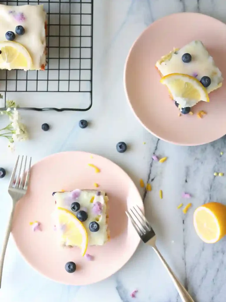 Lemon Blueberry Sheet Cake Recipe 2 Two slices of lemon blueberry sheet cake on pink plates topped with glaze, blueberries, and lemon slices