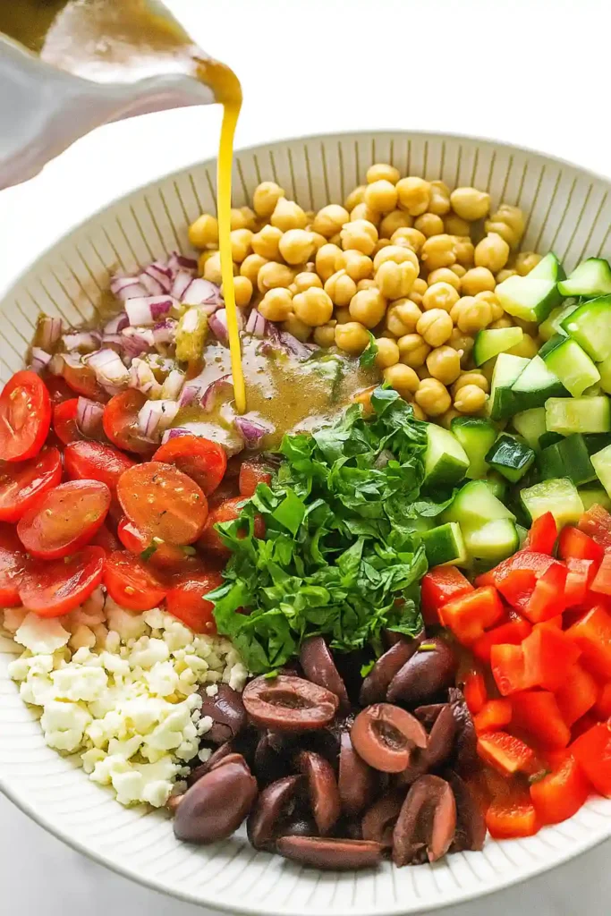 Easy Mediterranean Chickpea Salad Recipe Fresh and Quick 4 Dressing being poured onto Mediterranean chickpea salad with colorful fresh vegetables and chickpeas