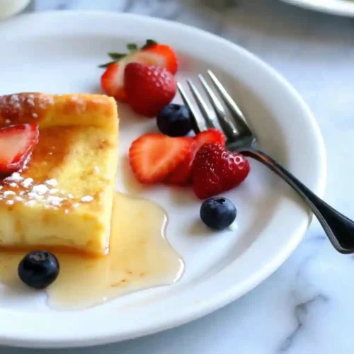 Fluffy German Pancakes Recipe 5 German Pancakes slice served with syrup, blueberries, and strawberries on a plate