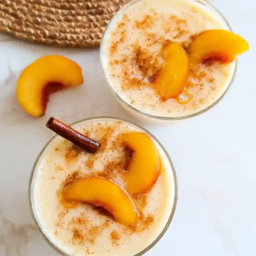 Creamy Peach Smoothie (No Sugar Needed) 7 Two glasses of peach smoothie topped with cinnamon and peach slices on marble