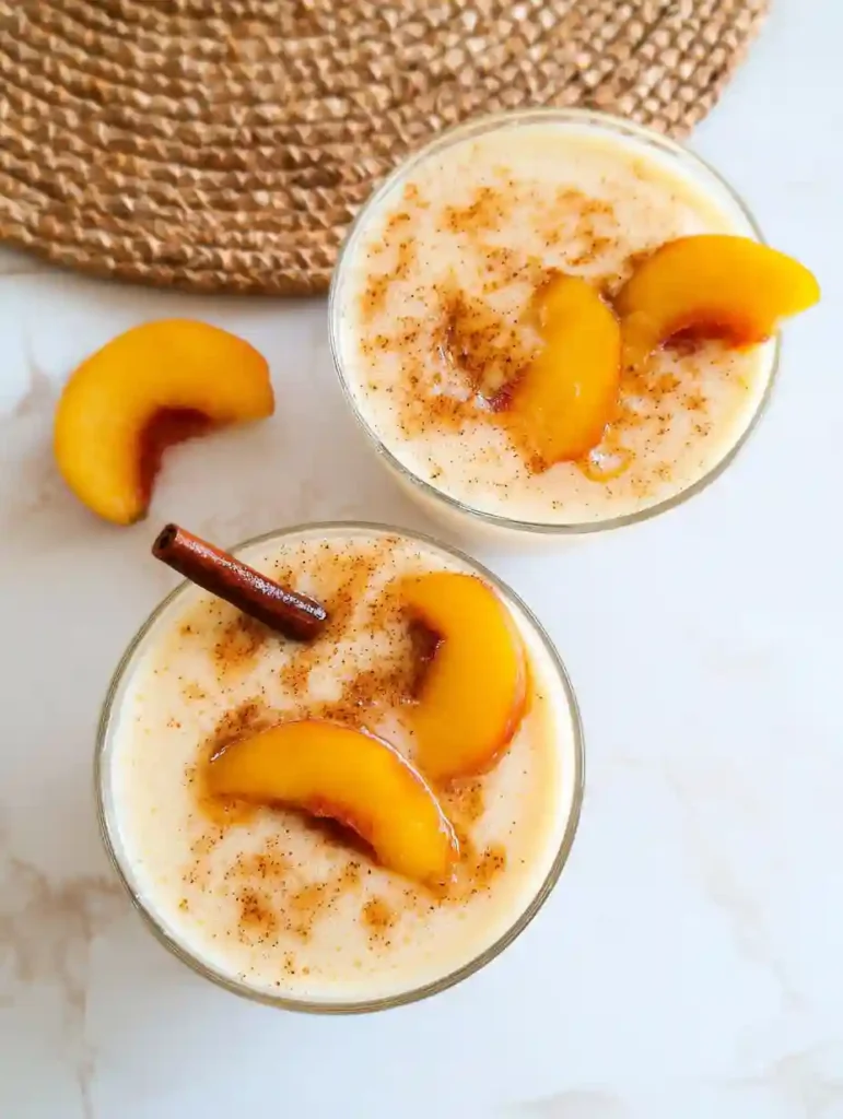 Creamy Peach Smoothie (No Sugar Needed) 5 Two glasses of peach smoothie topped with cinnamon and peach slices on marble