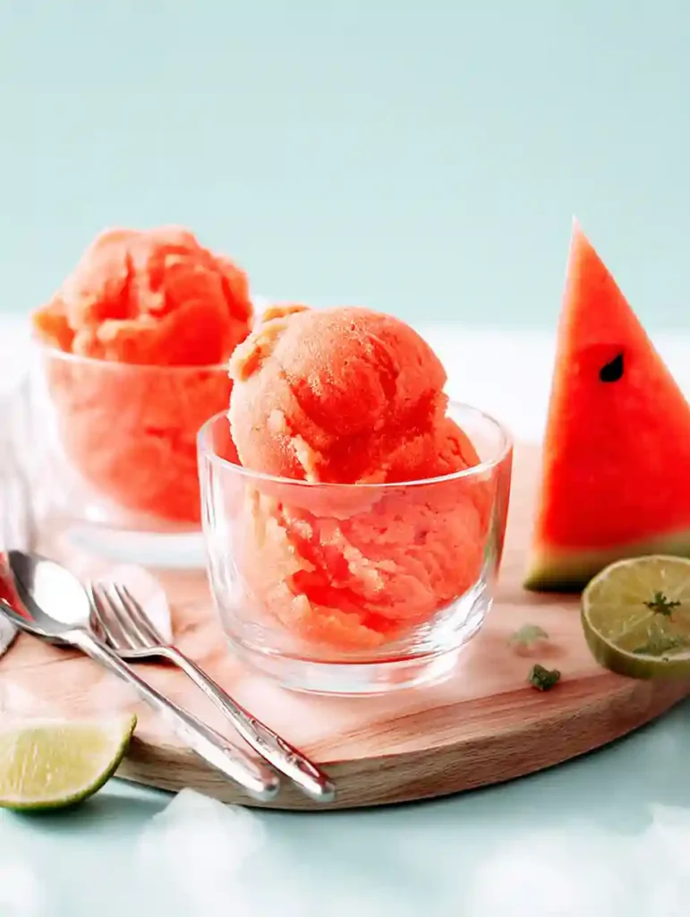 5-Minute Watermelon Sorbet 6 Two glass bowls filled with scooped watermelon sorbet beside fresh lime and watermelon slices