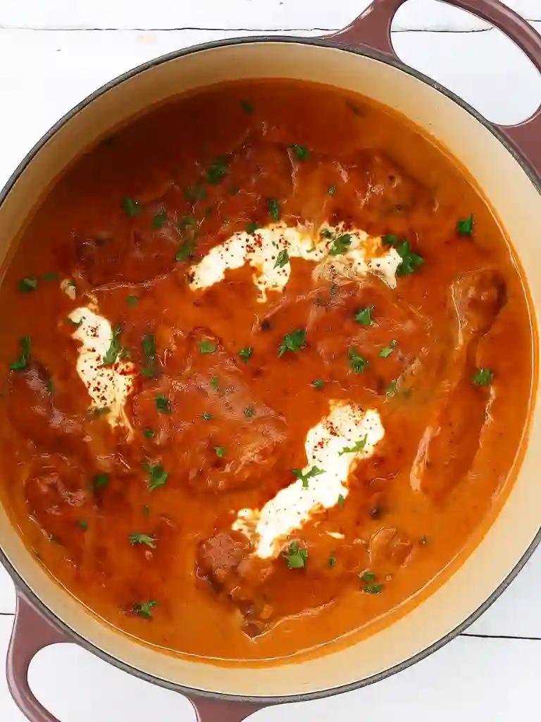 Authentic Chicken Paprikash Recipe 3 Chicken paprikash cooking in a Dutch oven with paprika cream sauce and fresh herbs