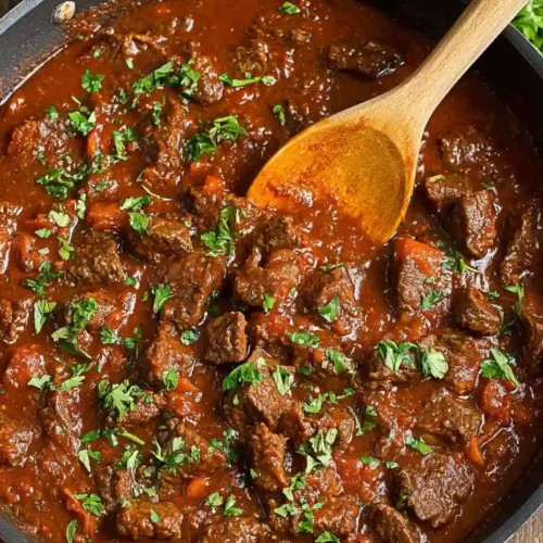 Irresistible Beef Goulash Recipe 6 Beef goulash simmering in a black pot with a wooden spoon and chopped parsley on top