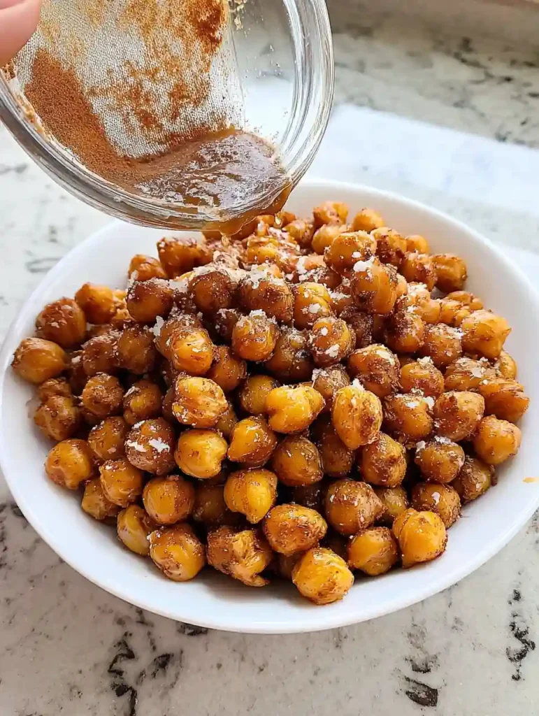 Crispy Roasted Chickpeas Snack 5 Crispy roasted chickpeas in a bowl being coated with cinnamon maple glaze from a glass dish