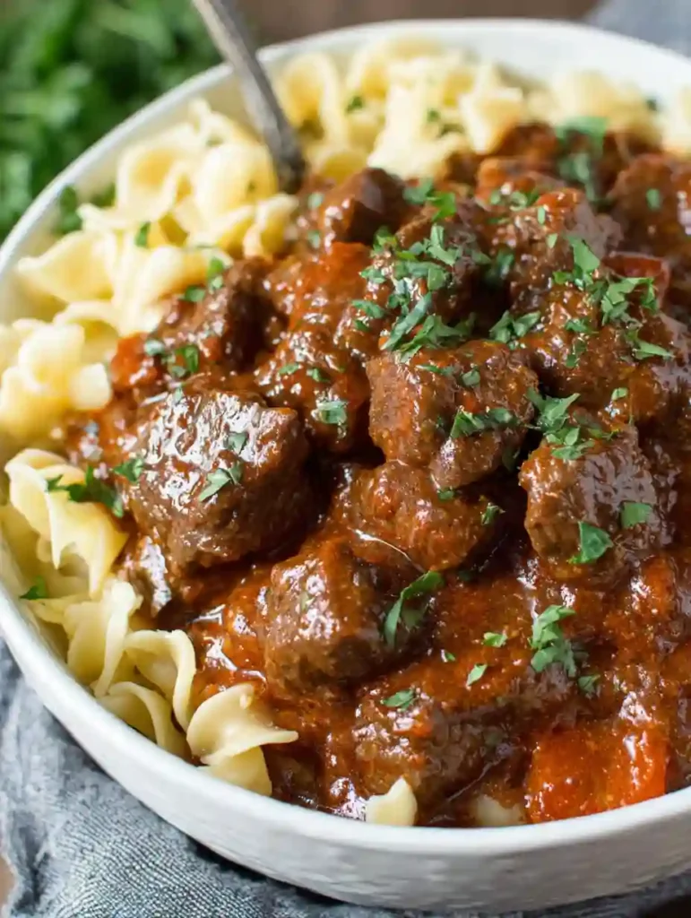 Irresistible Beef Goulash Recipe 4 Close-up of beef goulash served over egg noodles with thick paprika sauce and fresh parsley
