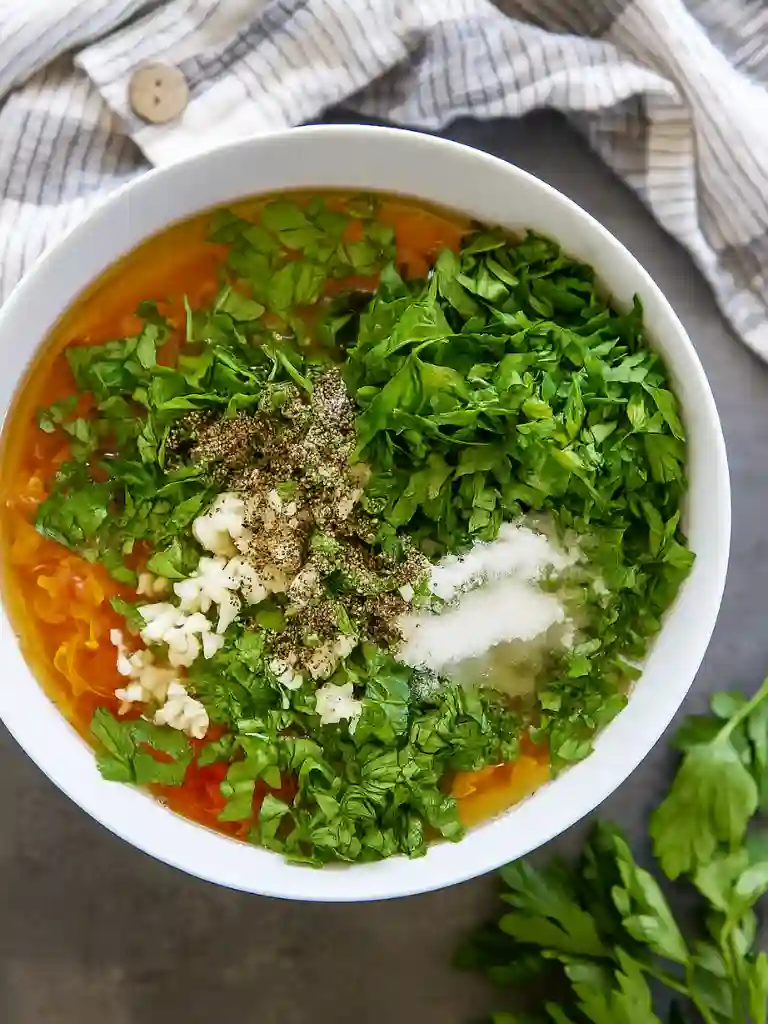 Chopped herbs, garlic, pepper, and salt on top of crushed tomatoes in a bowl for Margherita sauce