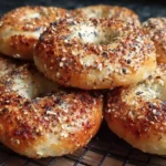 Close-up of golden sourdough discard bagels topped with everything seasoning on a cooling rack