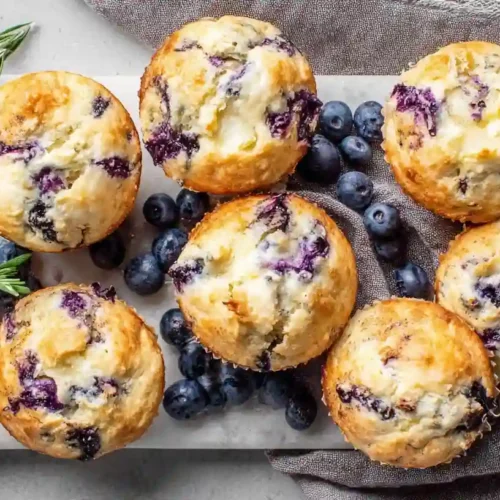 Irresistible Blueberry Cream Cheese Muffins 4 Blueberry Cream Cheese Muffins with golden tops and fresh berries on a serving board