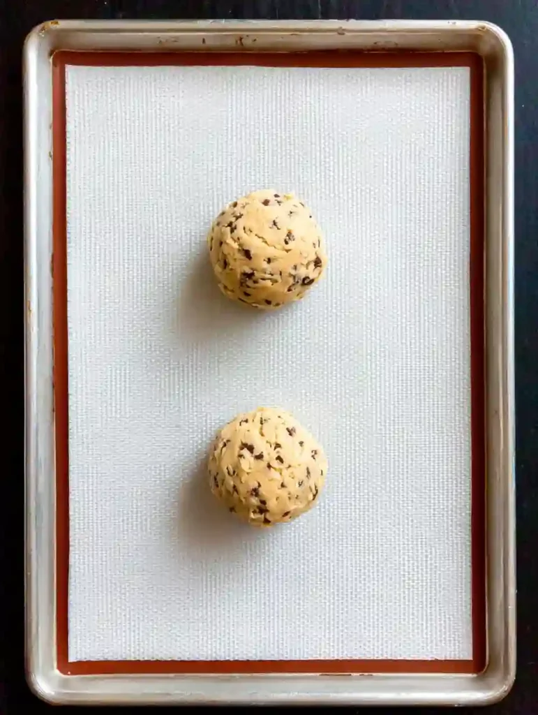 Giant Chocolate Chip Cookie Recipe 2 Unbaked giant chocolate chip cookie dough balls spaced on a baking sheet