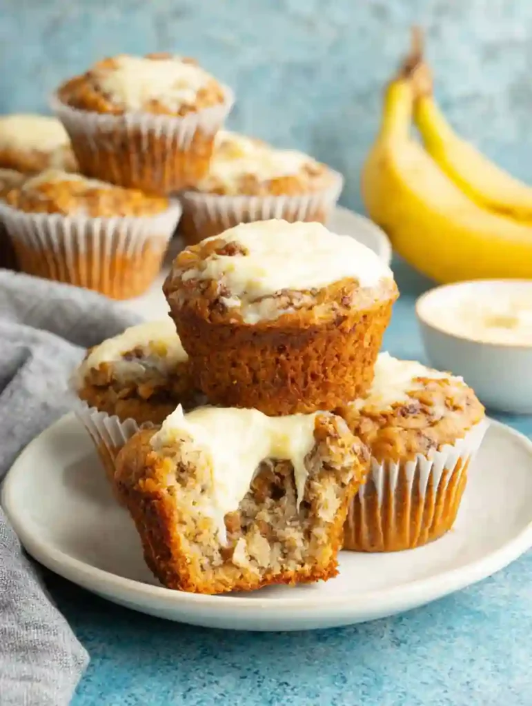 Banana Cream Cheese Muffins Recipe 2 Banana Cream Cheese Muffins with creamy filling and ripe bananas in the background