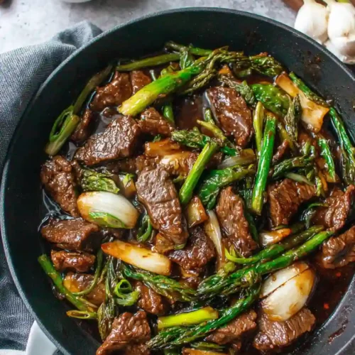 Beef with Oyster Sauce Recipe 4 Beef with Oyster Sauce stir fry with asparagus and onions in a black skillet