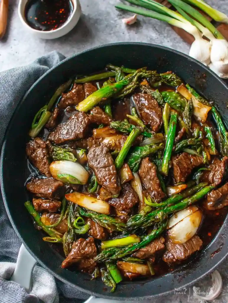 Beef with Oyster Sauce Recipe 2 Beef with Oyster Sauce stir fry with asparagus and onions in a black skillet