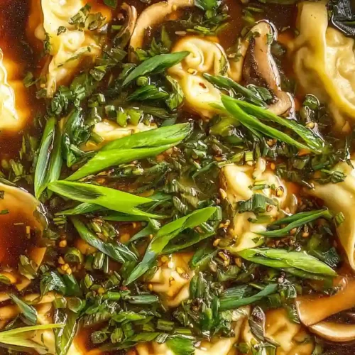 Gyoza soup topped with fresh herbs in a light soy broth