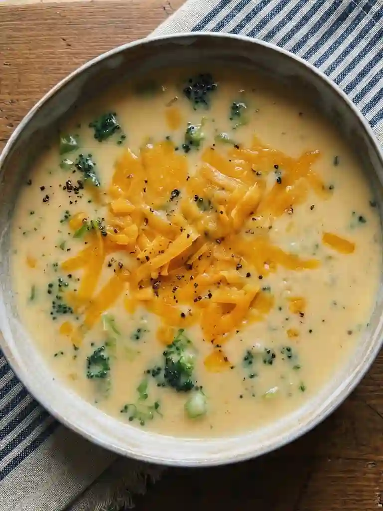 Close up of creamy Broccoli Cheddar Soup topped with shredded cheddar and black pepper