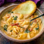 Bowl of creamy Marry Me Chicken Soup with pasta, spinach, sun dried tomatoes and toasted bread on wooden table