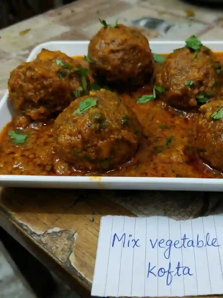Mix Vegetable Koftay Recipe 2 Closeup of Mix Vegetable Koftay balls in thick orange curry on a white plate, garnished with fresh coriander leaves