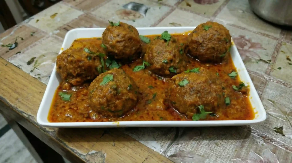 Mix Vegetable Koftay served in spicy tomato yogurt gravy on a white rectangular plate, garnished with fresh coriander