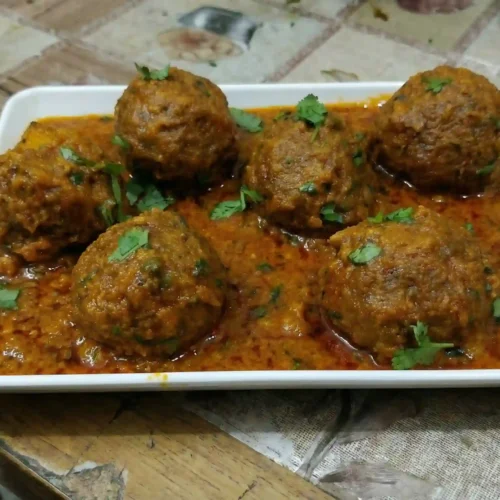 Mix Vegetable Koftay Recipe 3 Mix Vegetable Koftay served in spicy tomato yogurt gravy on a white rectangular plate, garnished with fresh coriander