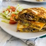 Hamburger Quesadilla sliced and stacked with ground beef and melted cheese on a white plate