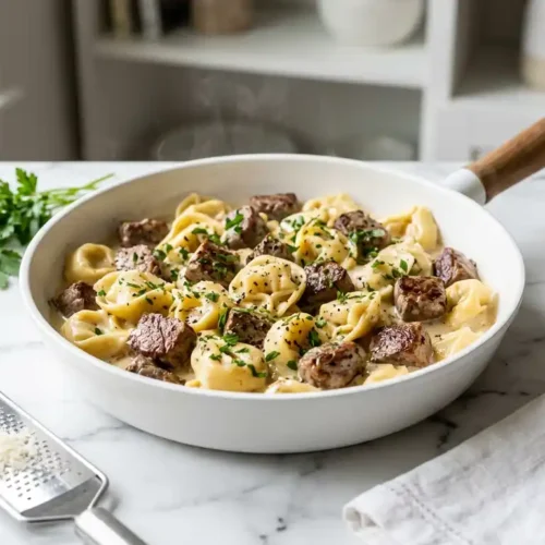 garlic steak tortellini in creamy Parmesan sauce with seared steak bites in a white skillet on marble