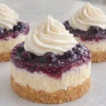 Mini Lemon Blueberry Cheesecakes with graham crust, blueberry topping, and whipped cream on a white plate