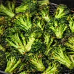 Air fryer broccoli florets crisping in basket with golden edges