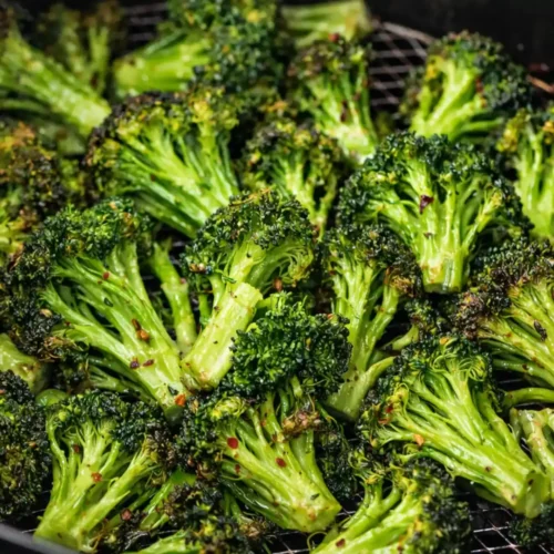 Air fryer broccoli florets crisping in basket with golden edges