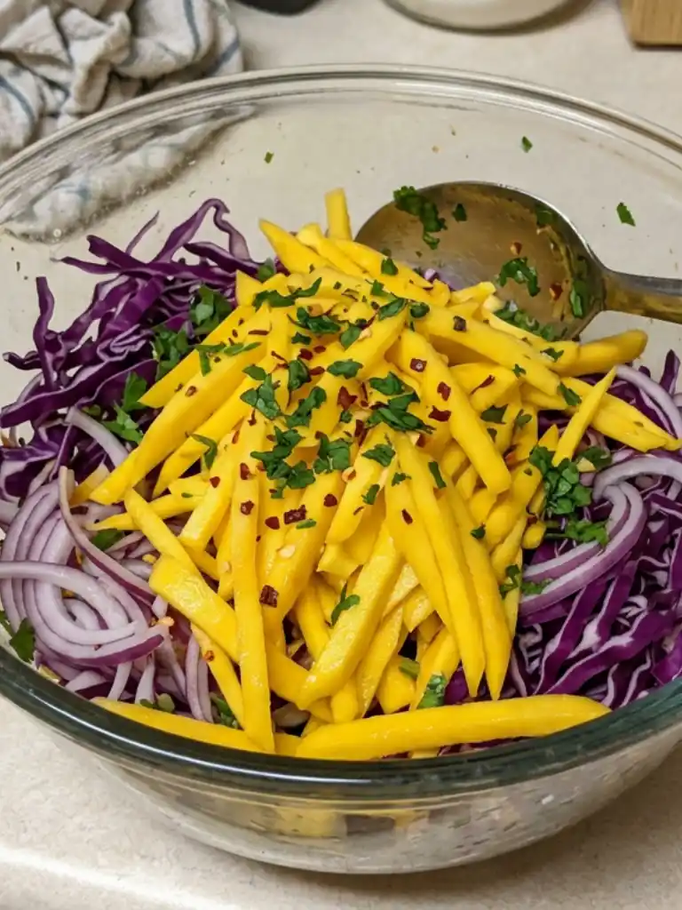 Fresh mango slaw with red cabbage, sliced onions, herbs, and chili flakes