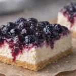 Creamy sugar-free cheesecake bars with almond crust and mixed berry topping on parchment paper