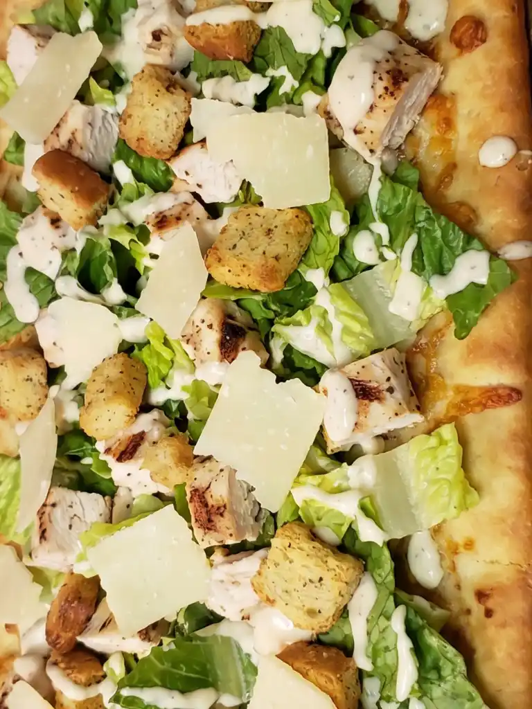 Chicken Caesar Flatbread close up with grilled chicken, romaine, Parmesan, croutons, and creamy Caesar drizzle