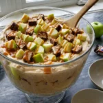 Snickers Apple Salad in glass bowl with green apples, chopped candy bars, and caramel drizzle