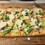 Chicken Caesar Flatbread topped with grilled chicken, romaine, Parmesan, croutons, and creamy dressing on crispy crust