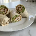 Chicken Caesar Wraps sliced in half with crispy chicken, romaine, and Caesar dressing on a white plate